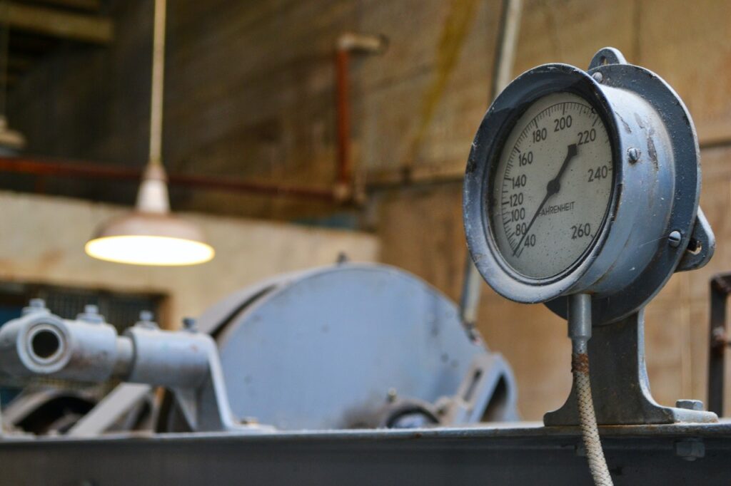 A white and gray manual gauge near a white hanging light in an old factory