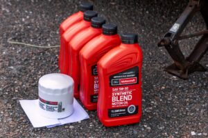 Five red bottles of Motorcraft Synthetic Blend motor oil beside a white oil filter on top of a white paper placed on the asphalt