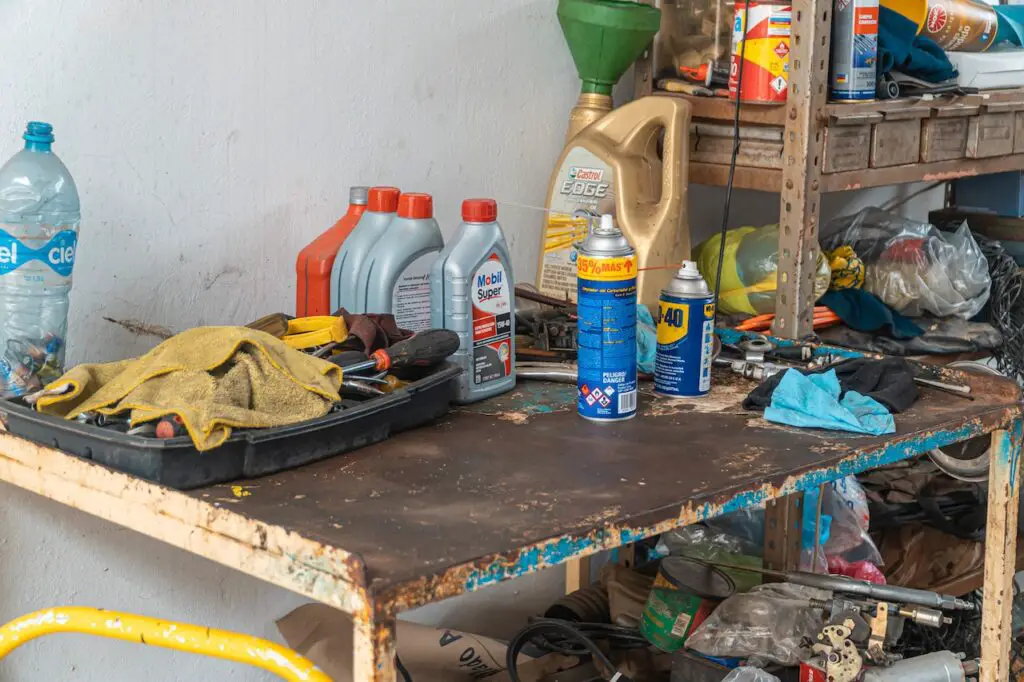 Various brands of motor oil and WD-40 placed near a tray of dirty hand tools on top of an old metal table