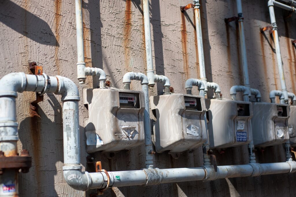 A long gray water line with a dirty water meter is placed on a rough wall