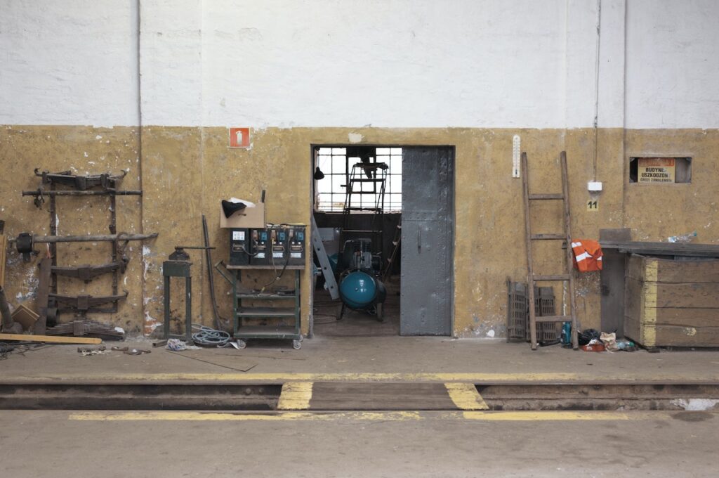 A blue air compressor is stored in an unorganized room near the dirty workshop