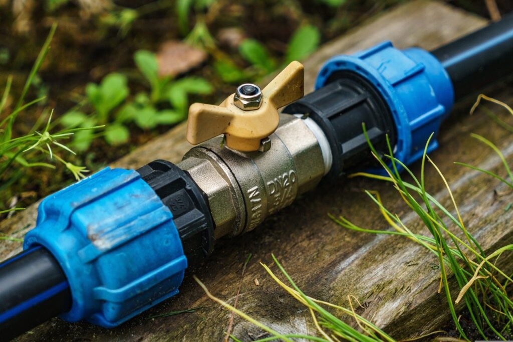 A blue and black pipeline with a yellow knob on top of wet wood near the green grass