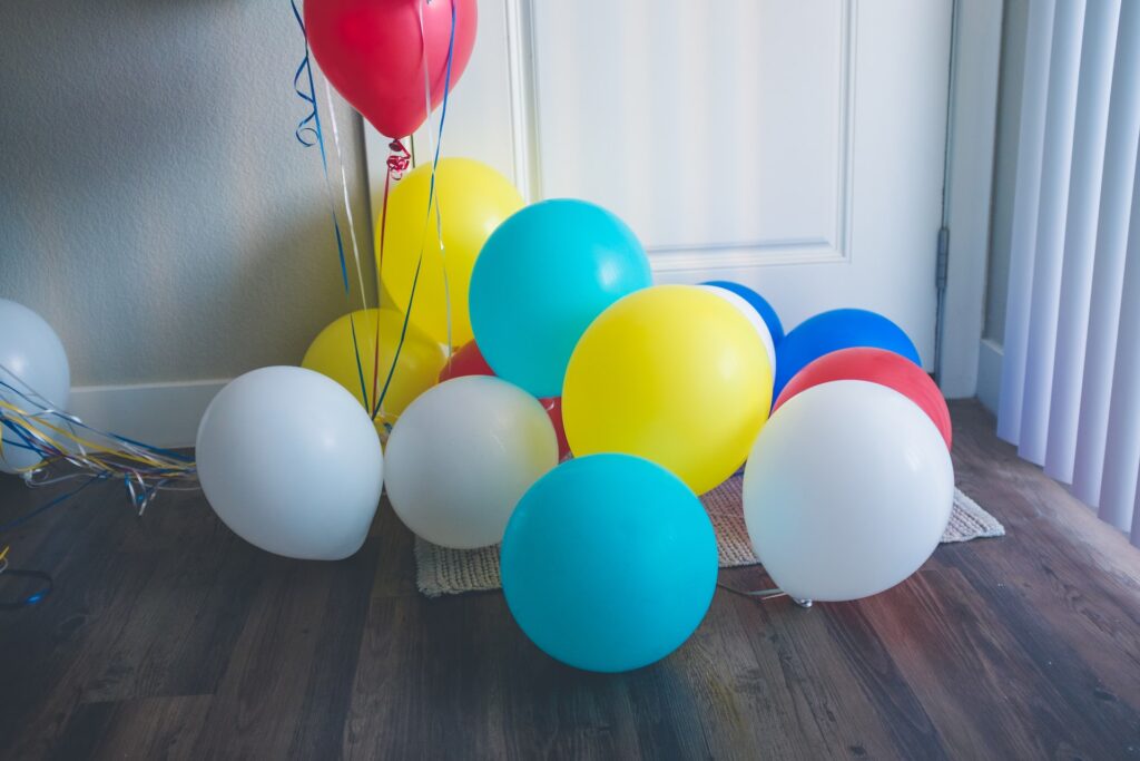 Different colored balloons on top of a gray rug are placed near a white door in a room with a brown wooden floor
