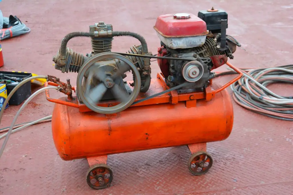 An orange compressor near a black and yellow toolbox on top of a red metal floor