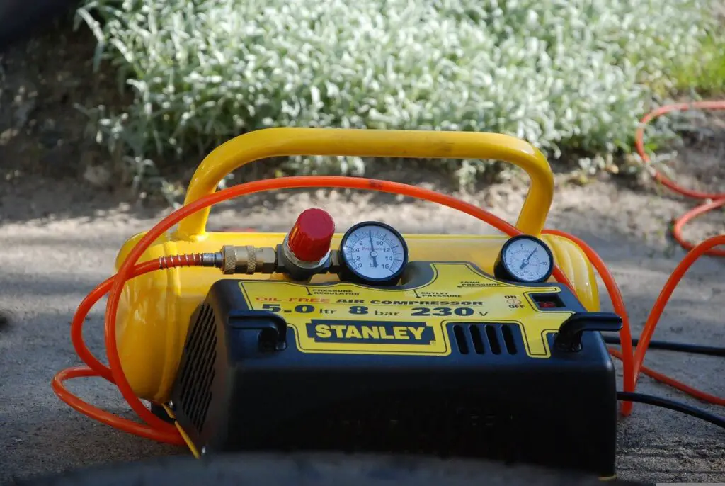 A yellow and black air compressor with an orange tube placed on top of a black asphalt