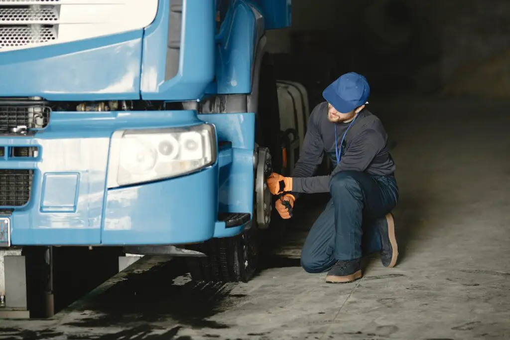 A man in a blue cap and a blue jumper is repairing a blue truck's black wheel inside an auto repair shop