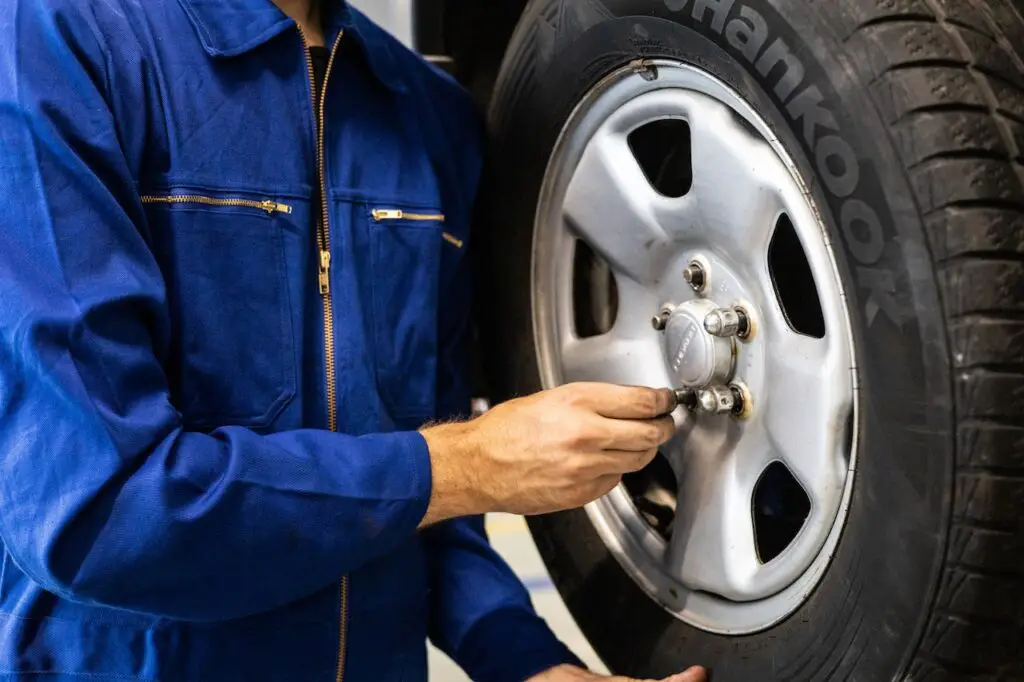 A person wearing a blue jumpsuit is holding black tire and silver lug nuts at a car repair shop