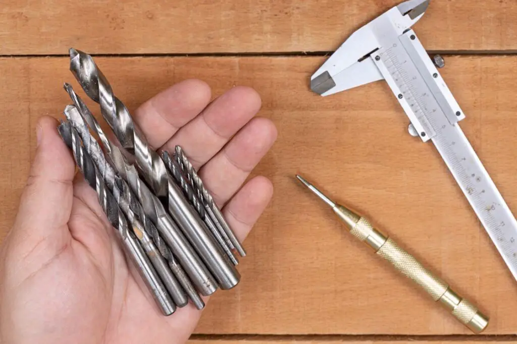 Hand holding different kinds of drill bits with a T-square on the table