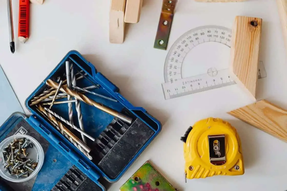 Drill bits, screws, protractor, and measuring tape placed on top of a table