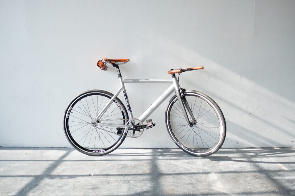 A white and brown colored bike leaning against a white wall on a gray concrete floor