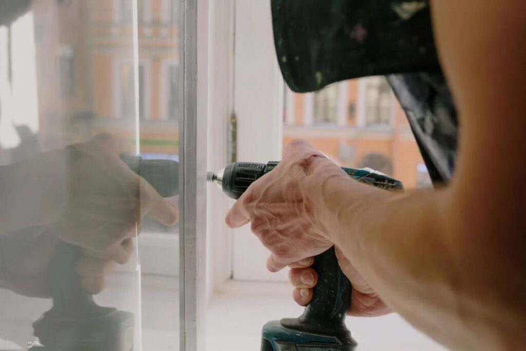 Man screwing metal detail on window with a drill