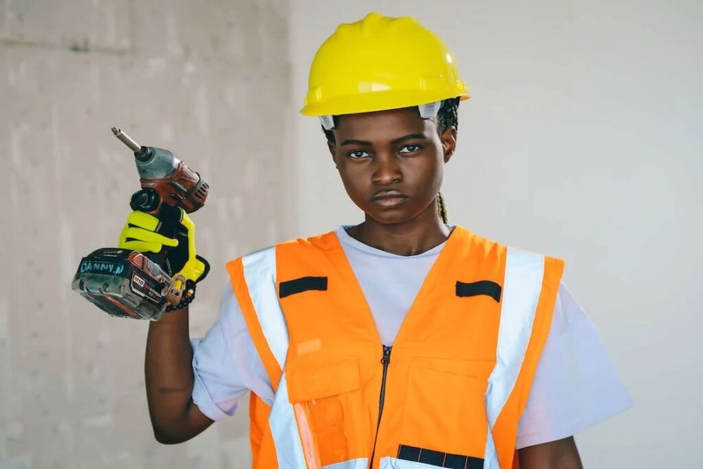 Woman in construction protective gear holding a cordless drill with her gloved hand