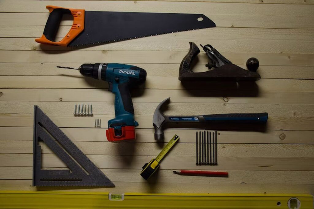 Drill, hammer, measuring tape and other tools laid neatly on a wooden table