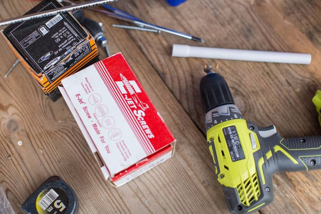 Drill, box of screws and other tools on a wooden table