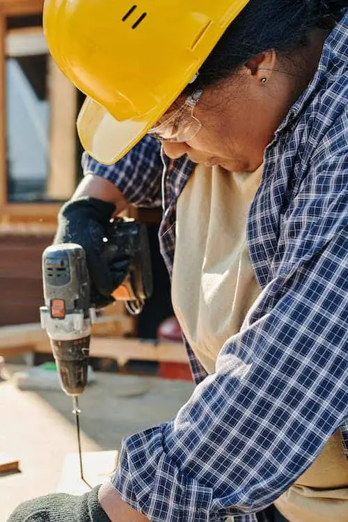 Woman wearing protective gear drilling a hole in a wood plank
