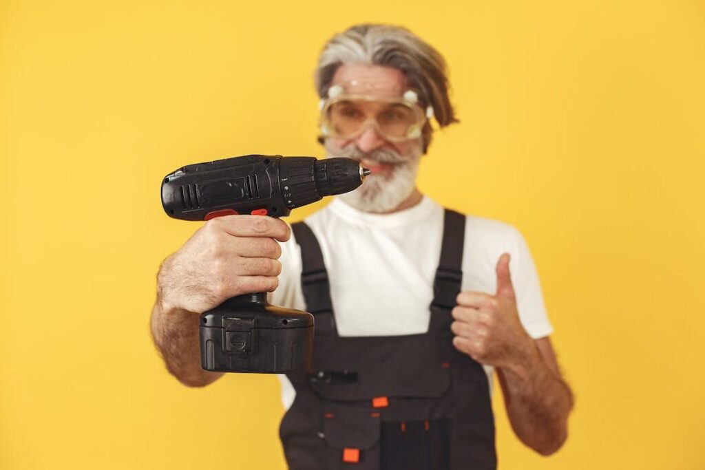 Man wearing black overalls doing a thumbs up while holding a cordless drill