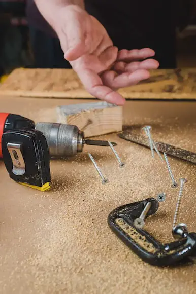 Hand tossing screws on a saw dust covered table that has his drill and other tools