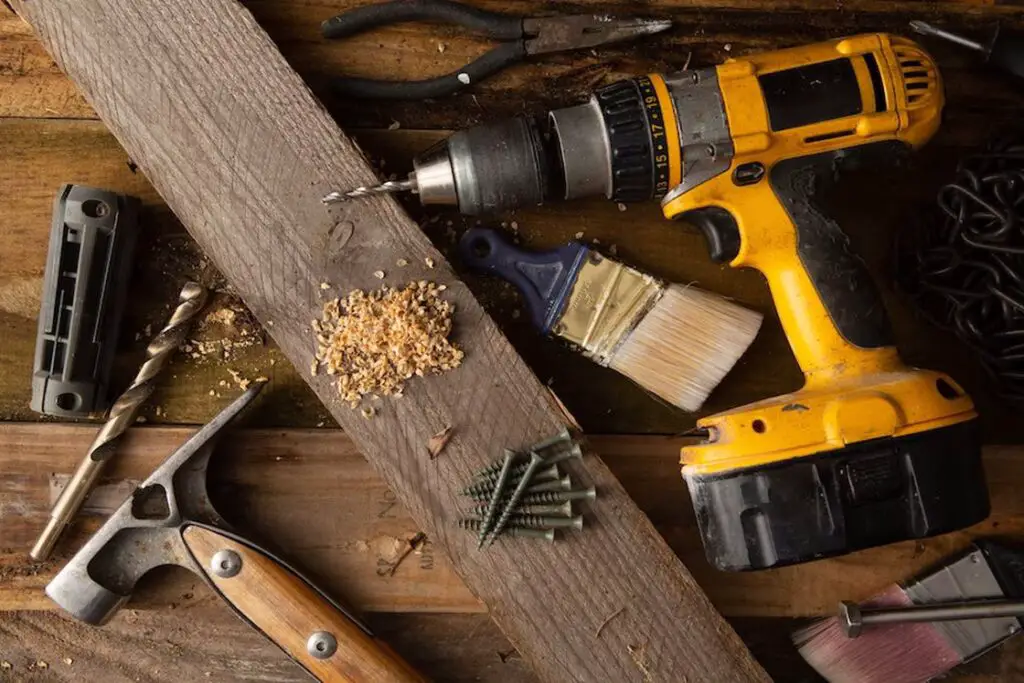Yellow cordless drill with nails, hammer and other tools laid out on a table