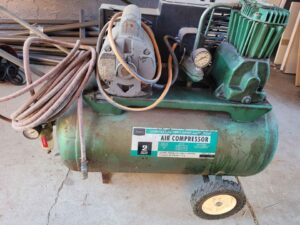 A green air compressor with an orange hose was placed on a gray floor
