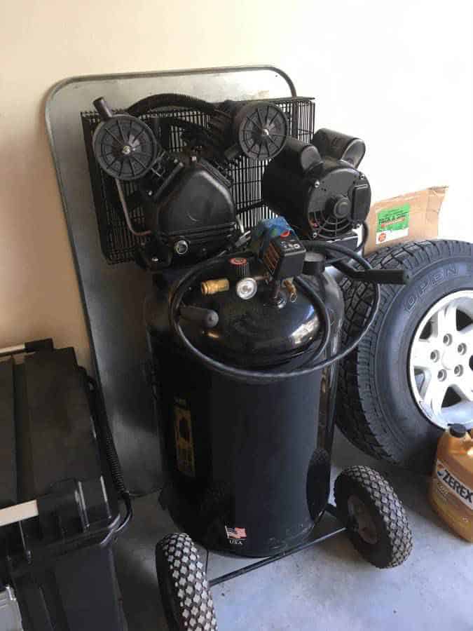 A black air compressor near a black tire and a black plastic container near the white wall