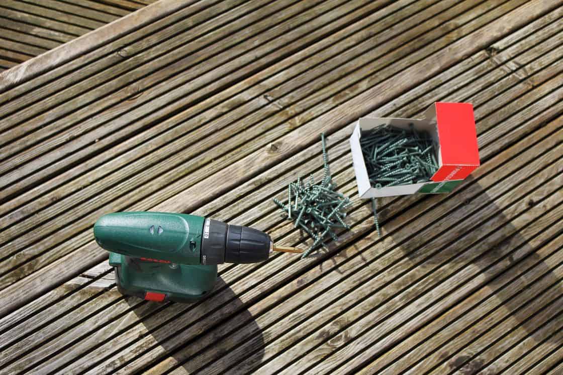 Drill with drill bit attached and an open box of screws on a wooden table