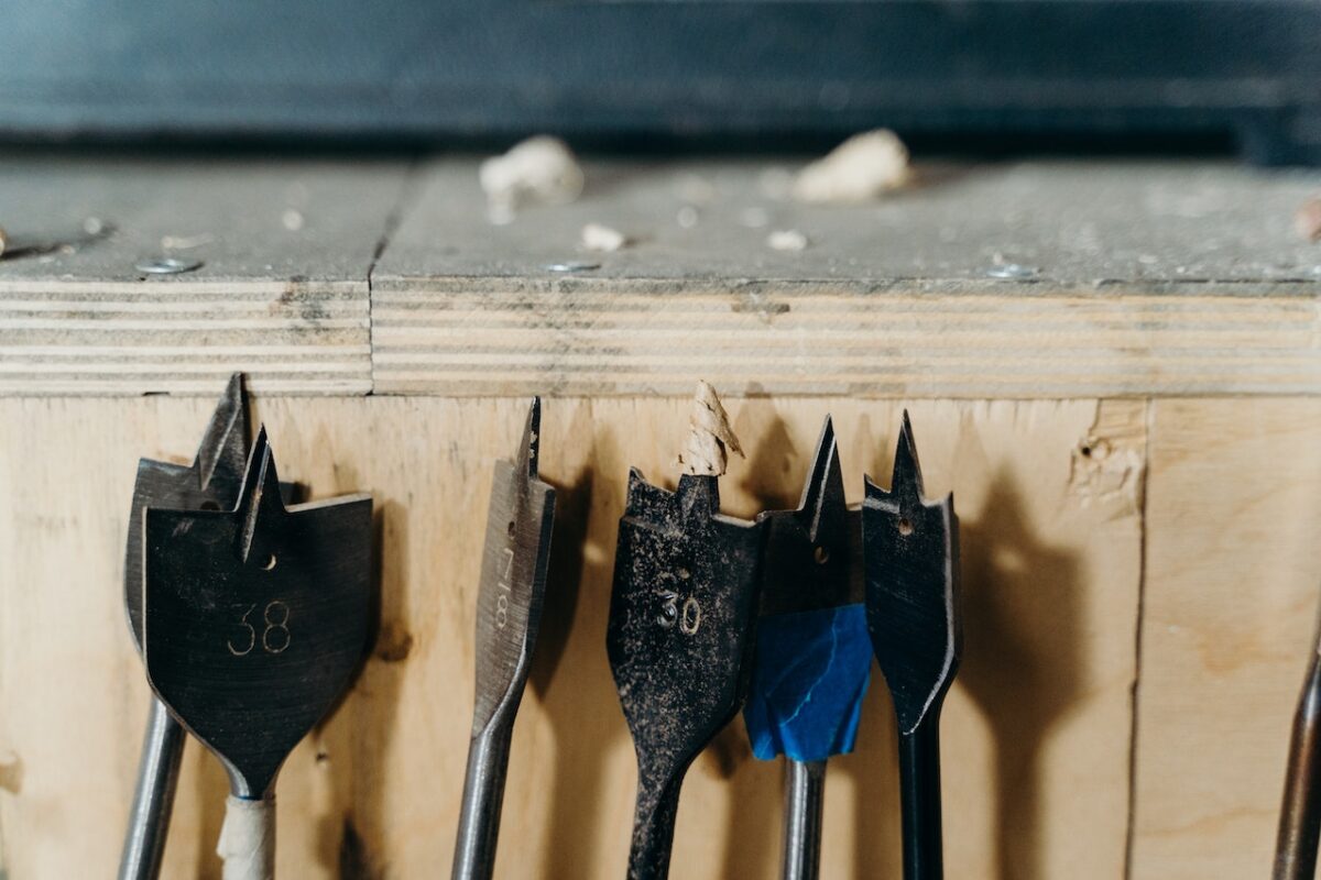 Different sizes of black drill bits with sharp pointy edges near a wooden wall