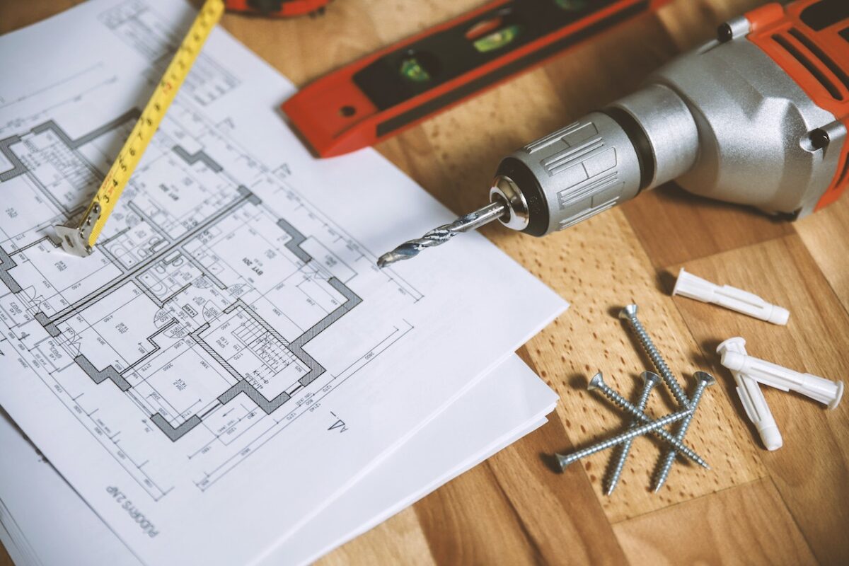 A drill bit attached to a drill and a floor plan placed on a wooden table