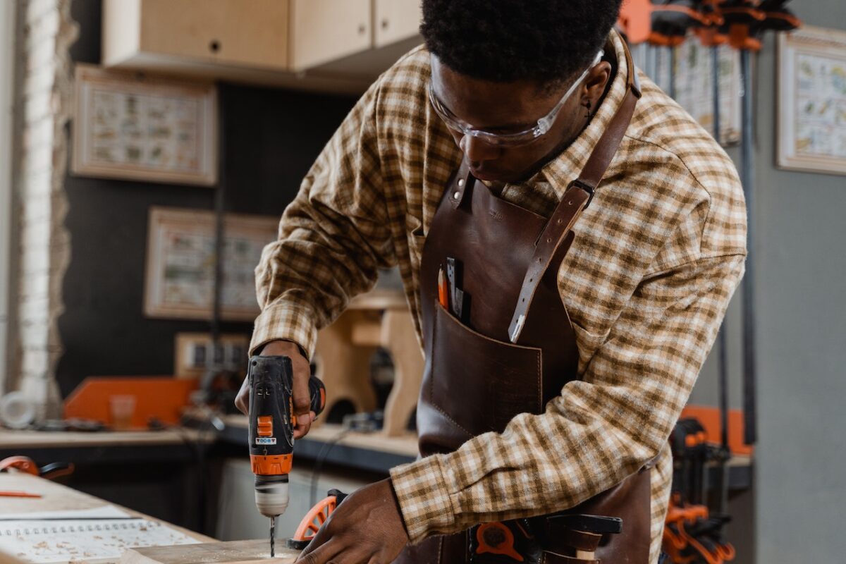 A man in checkered long sleeves using a drill with a drill bit