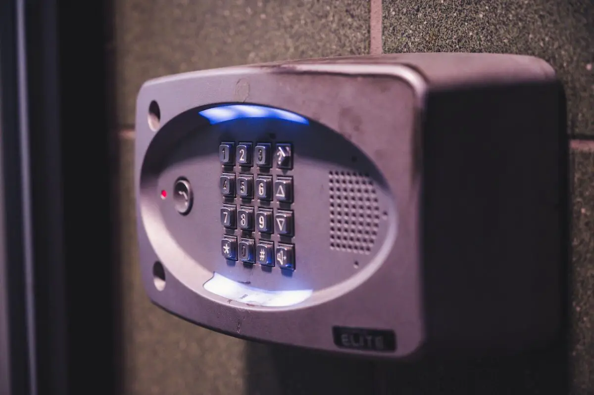 A silver doorbell with a gray keypad on a black tiled wall