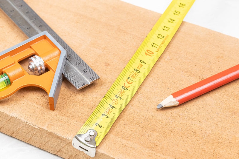 Measuring tape and combination square with an orange wooden pencil placed on the wooden board