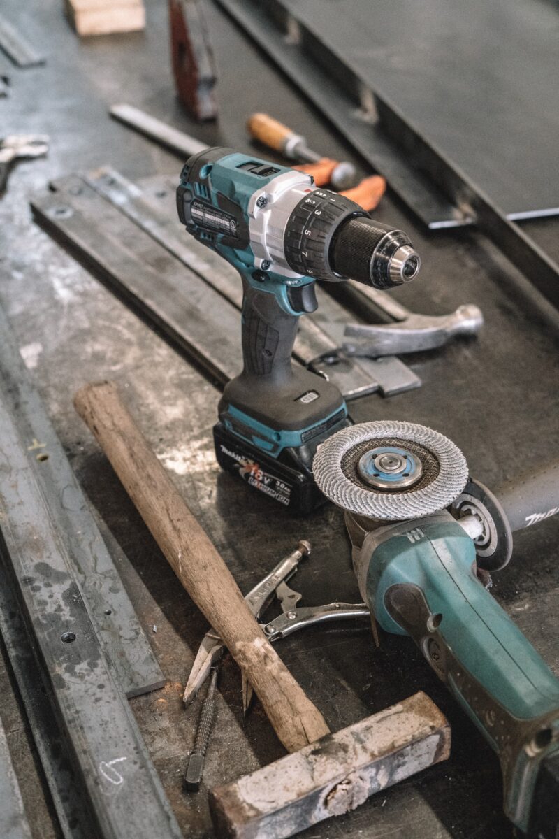 Green Makita cordless drill near angle grinder and different hammer