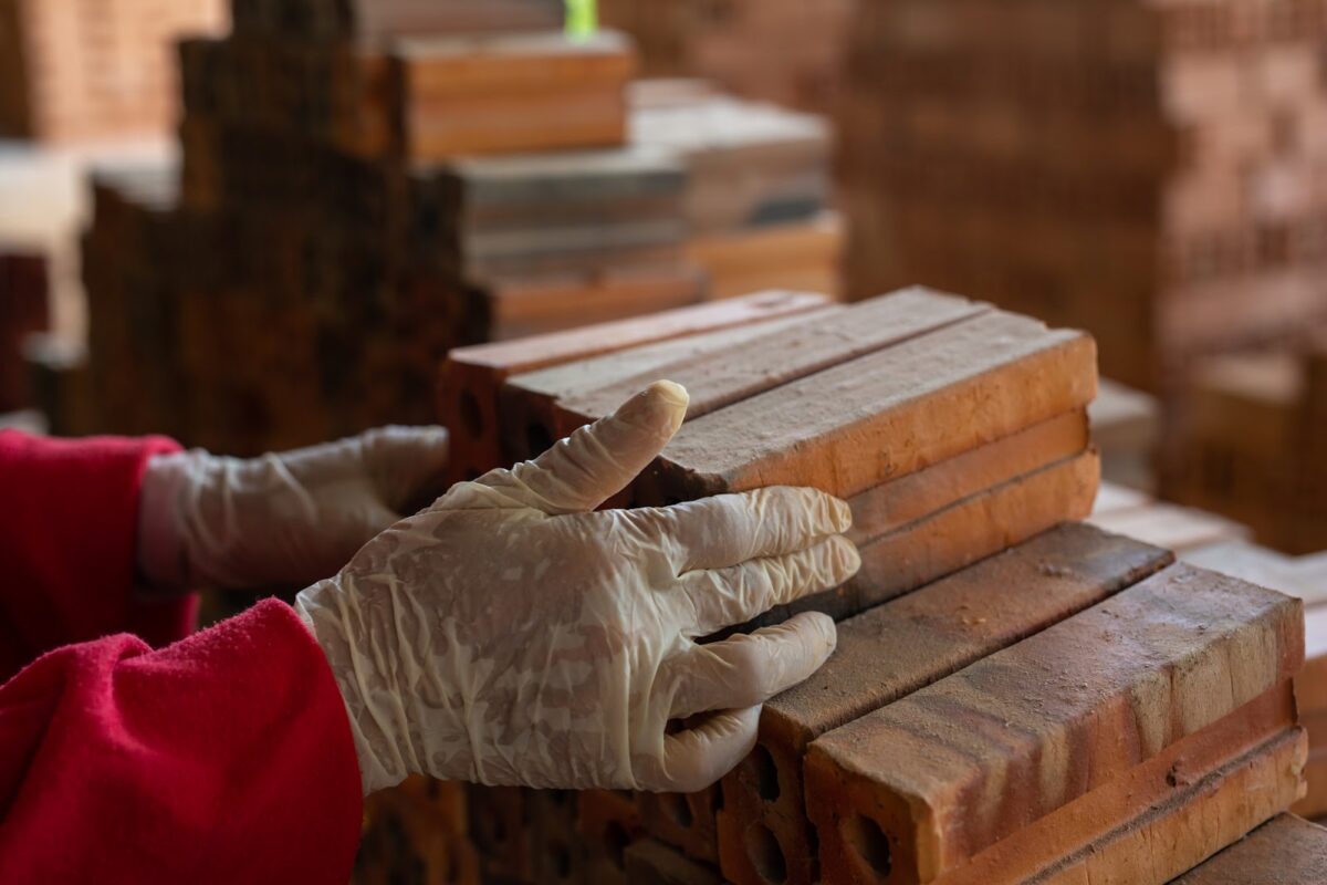 A person wearing red longs sleeves shirt and white latex gloves while stacking fire bricks