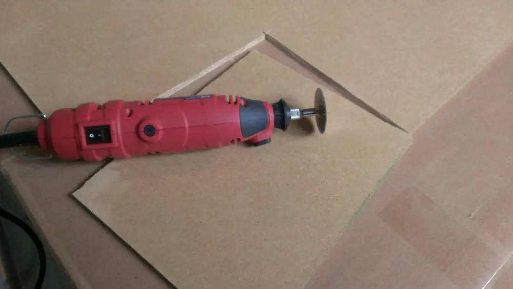 A red and black Dremel was used to cut a brown board on top of a brown table