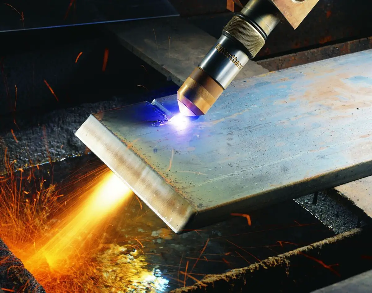 A person using a plasma torch with a bright yellow flame to cut silver steel on top of a black steel