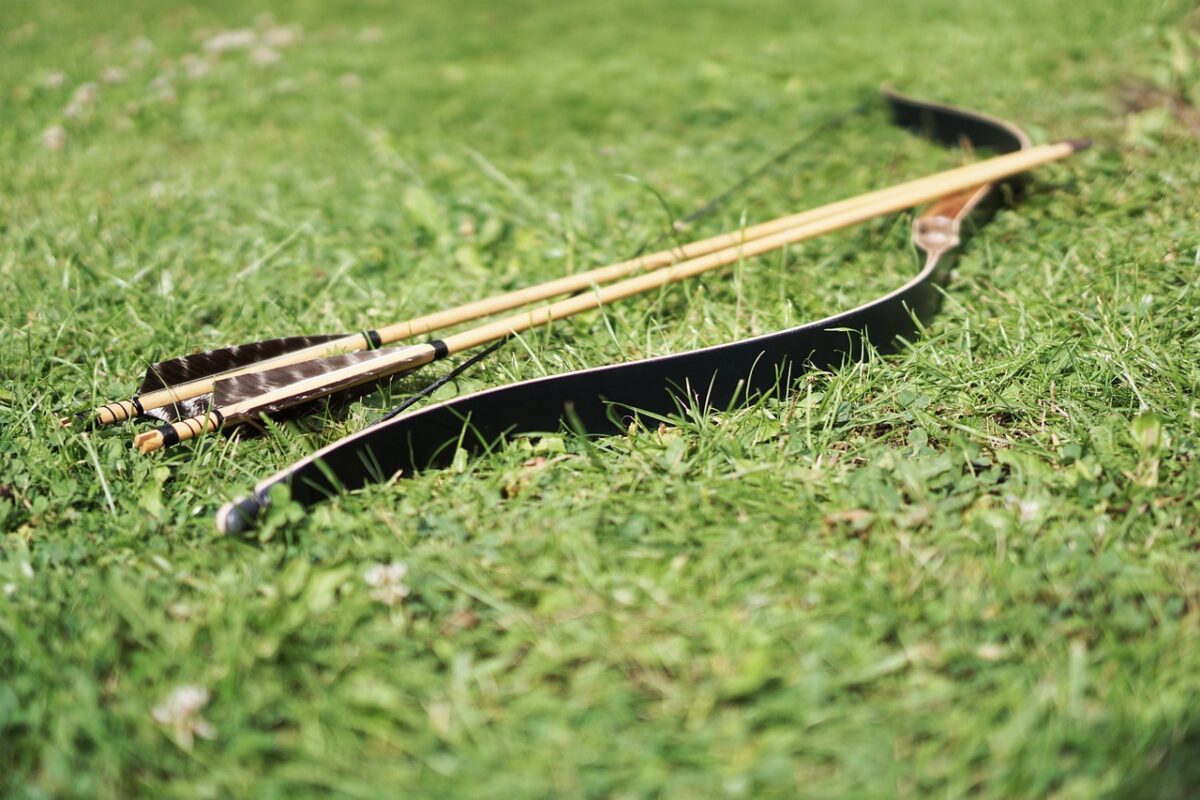 Archery arrows and a bow placed on the green grass