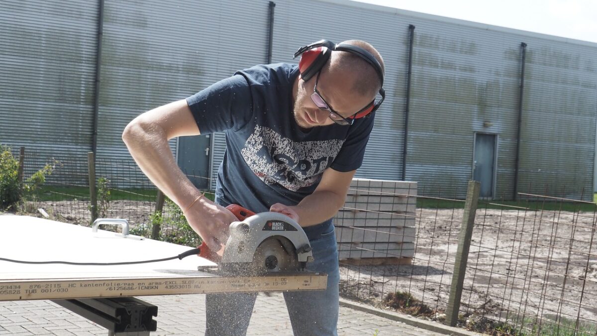A wood worker using a circular saw to cut a laminate in a workshop.