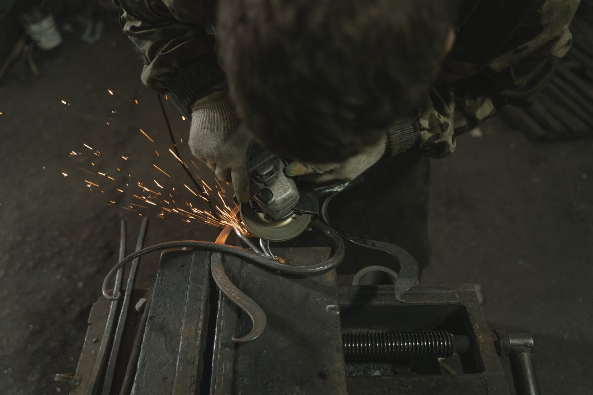 A man with a camouflage jacket and gloves using an angle grinder with a metal