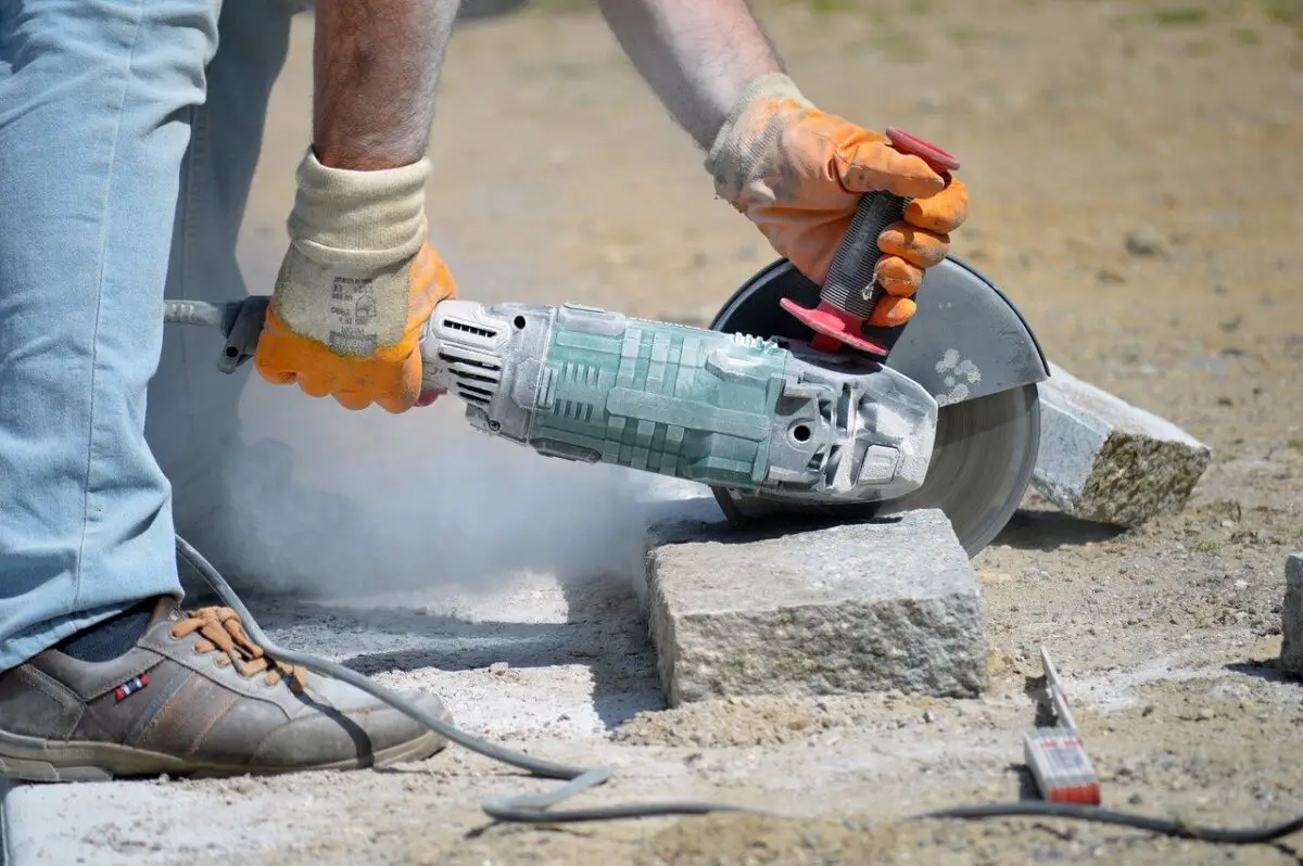 A green angle grinder slowly cutting a rock in a field.