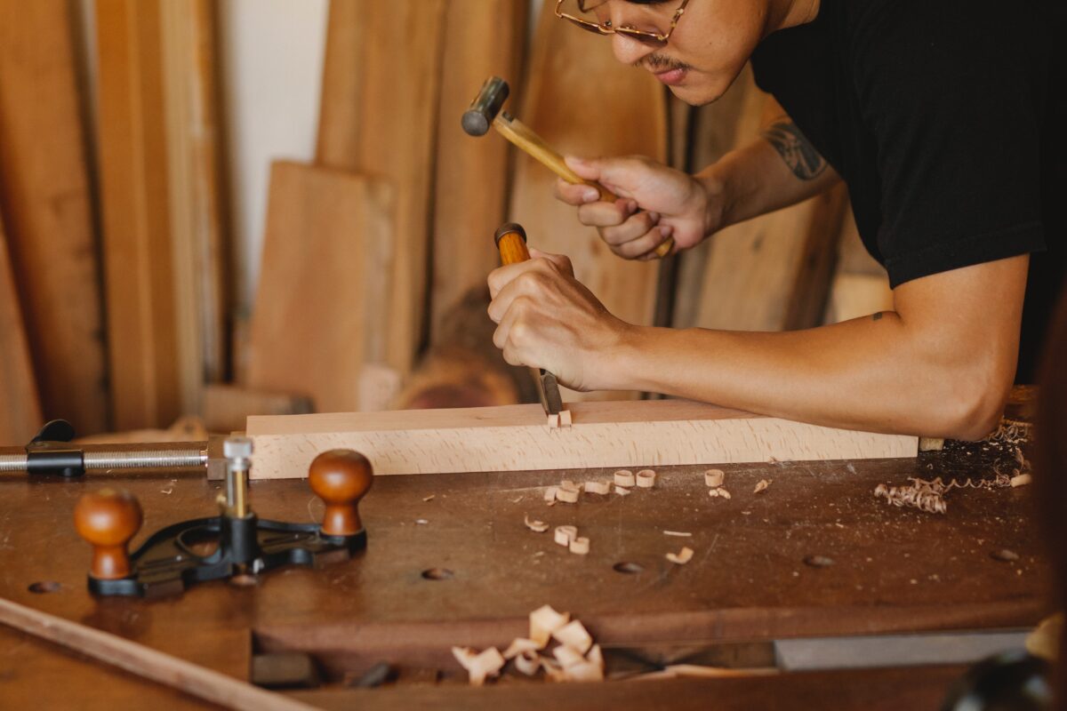 A man holding a mallet and chisel to slowly cut the wood