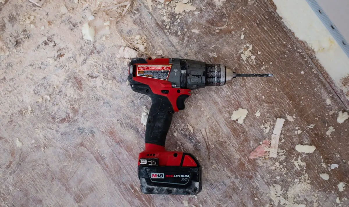 A M18 red lithium drill bit in a messy floor