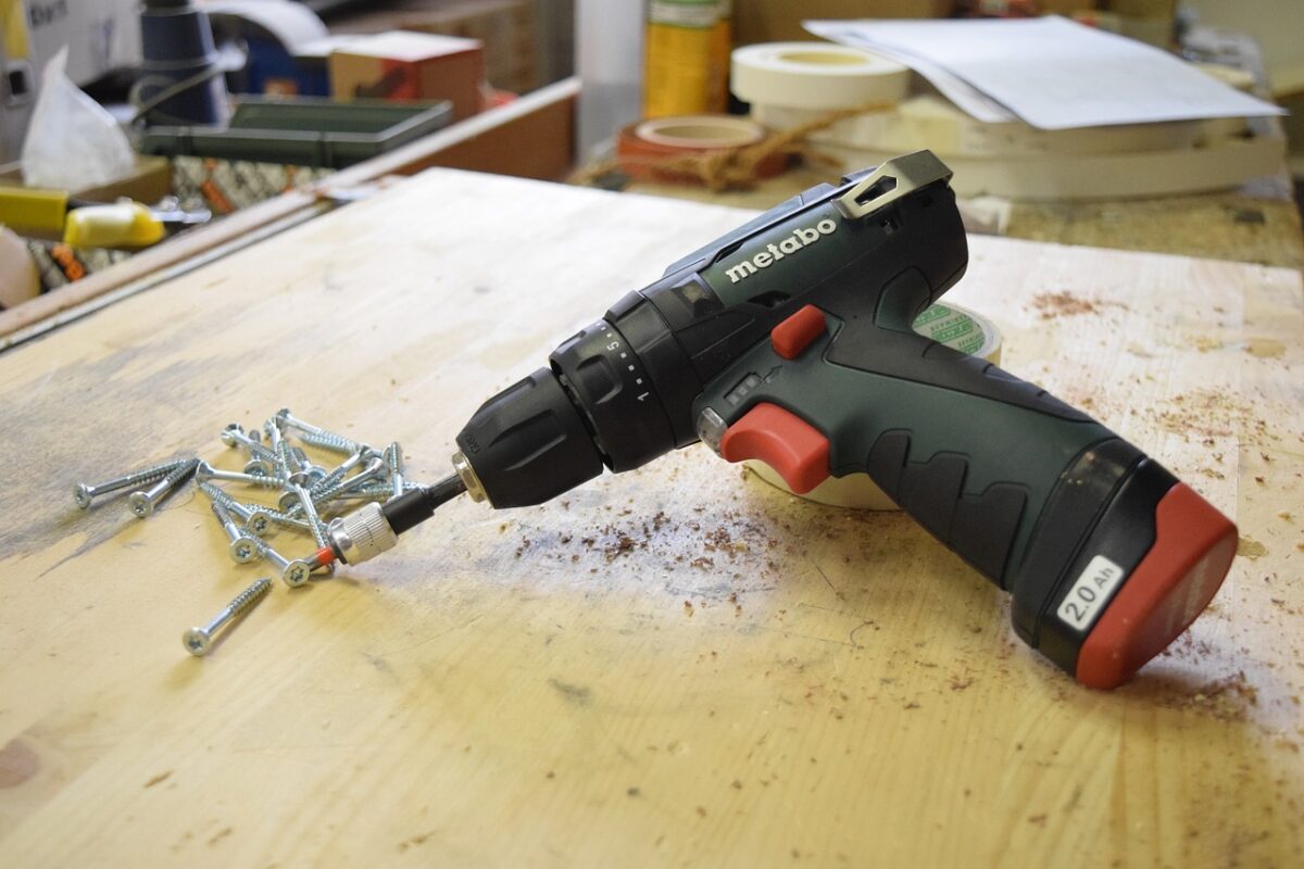 A drill leaning on a tape on a table with scattered screws